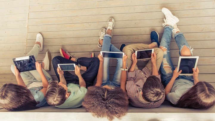 Jugendliche mit Tablets und Laptops am Boden sitzend